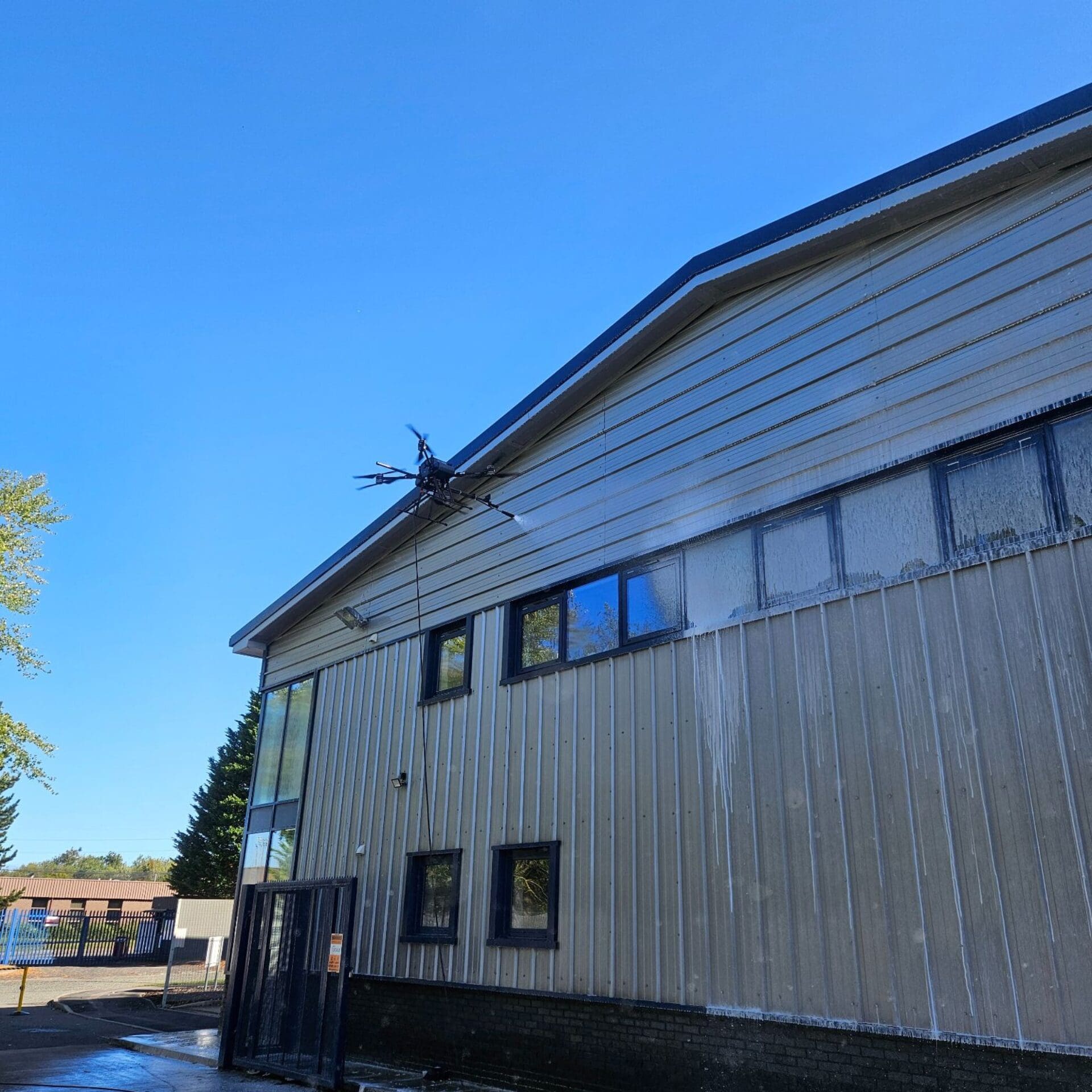 High-pressure drone cleaning in progress on warehouse cladding
